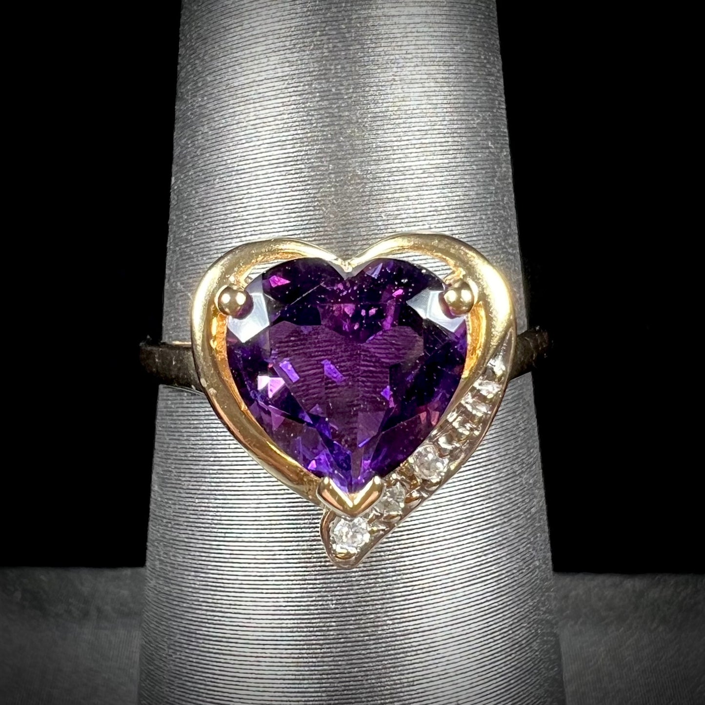 A ladies' yellow gold ring set with a heart shaped amethyst and round cut diamond accents.