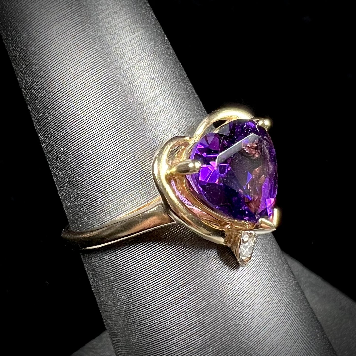 A ladies' yellow gold ring set with a heart shaped amethyst and round cut diamond accents.