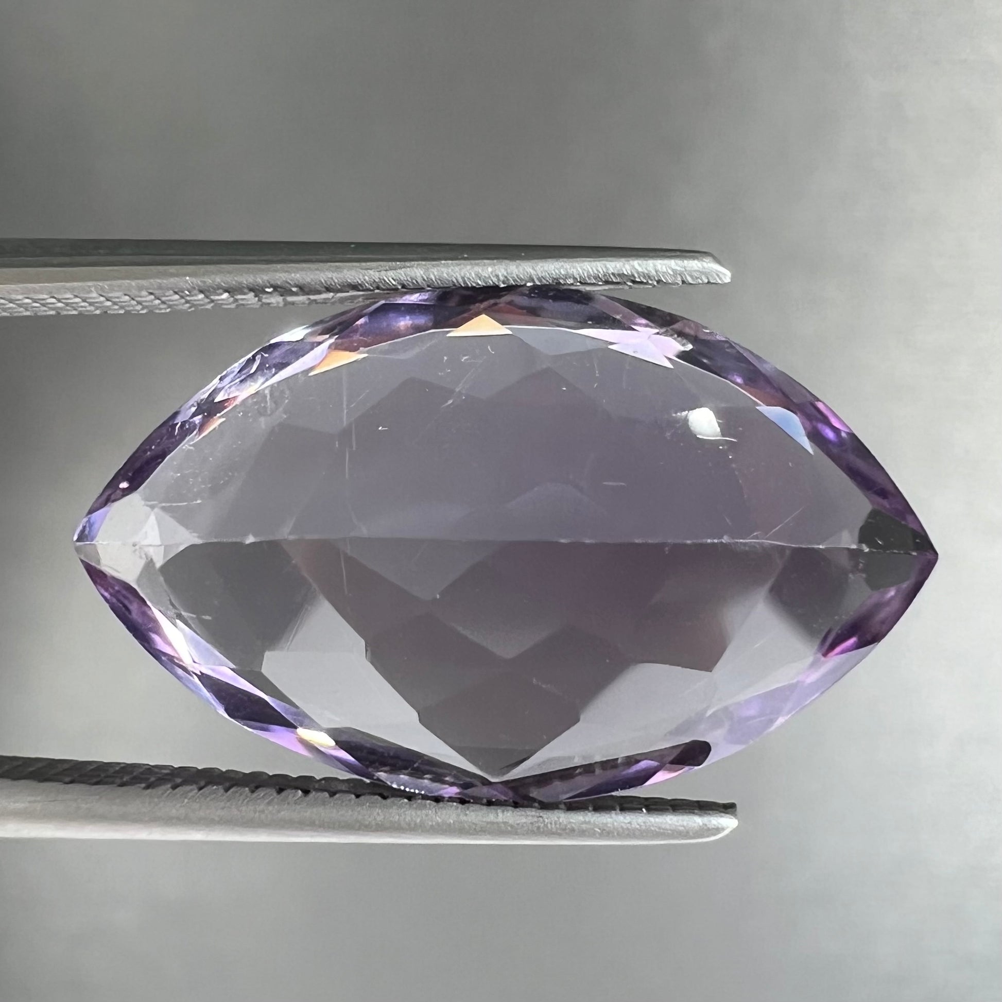 A loose marquise cut amethyst gemstone.  The stone is a light purple color and has scratches along the surface.