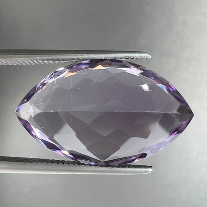 A loose marquise cut amethyst gemstone.  The stone is a light purple color and has scratches along the surface.