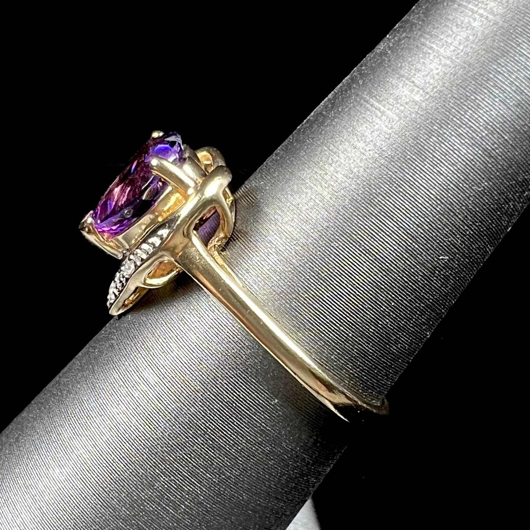 A ladies' yellow gold ring set with a heart shaped amethyst and round cut diamond accents.