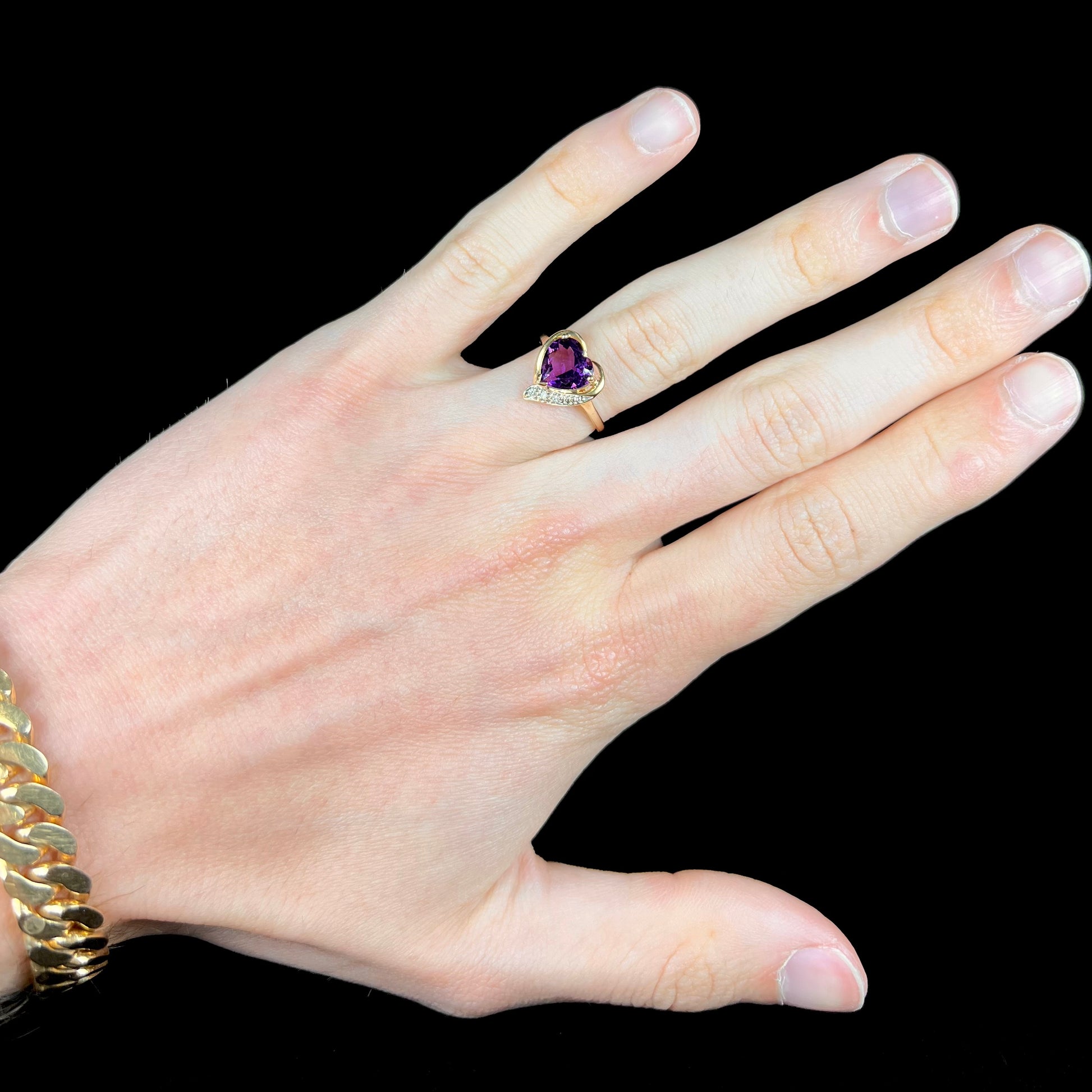 A ladies' yellow gold ring set with a heart shaped amethyst and round cut diamond accents.