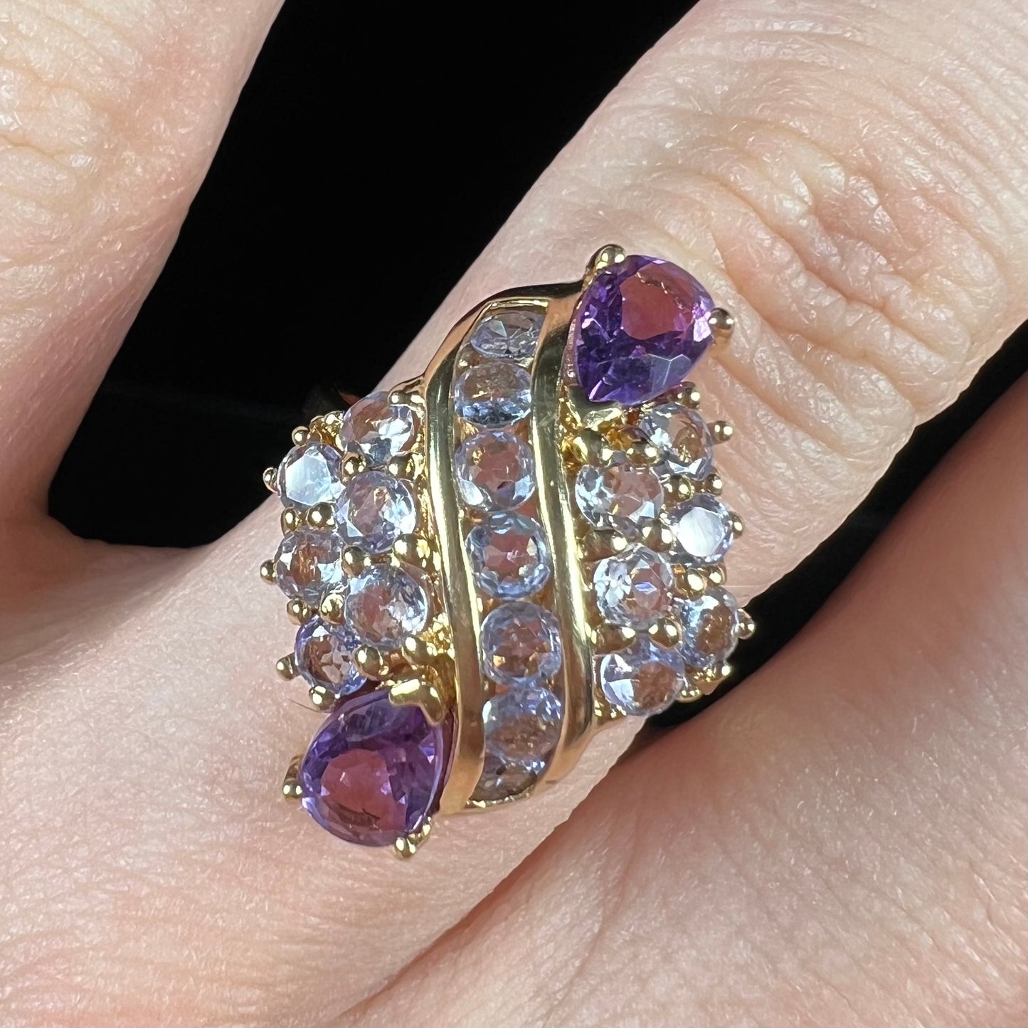 A ladies' gold ring set with a cluster of round tanzanites and two pear shaped amethyst accent stones.