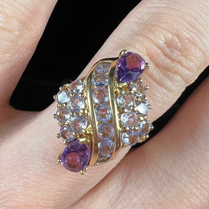 A ladies' gold ring set with a cluster of round tanzanites and two pear shaped amethyst accent stones.