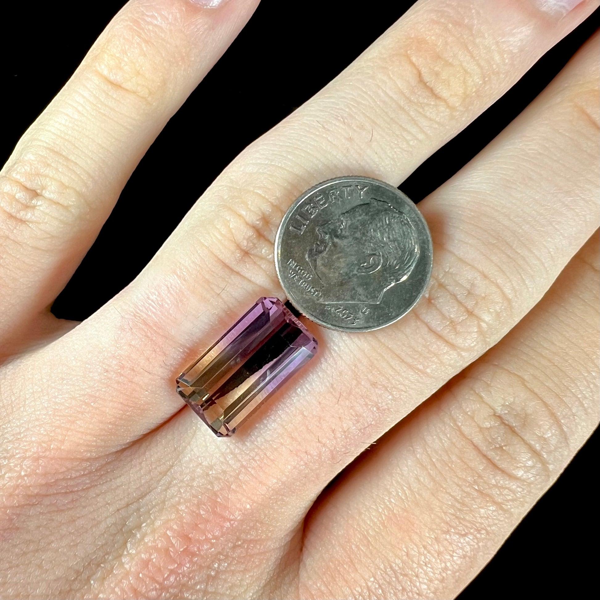 A loose, emerald cut ametrine stone.  The color fades from light purple to light yellow.