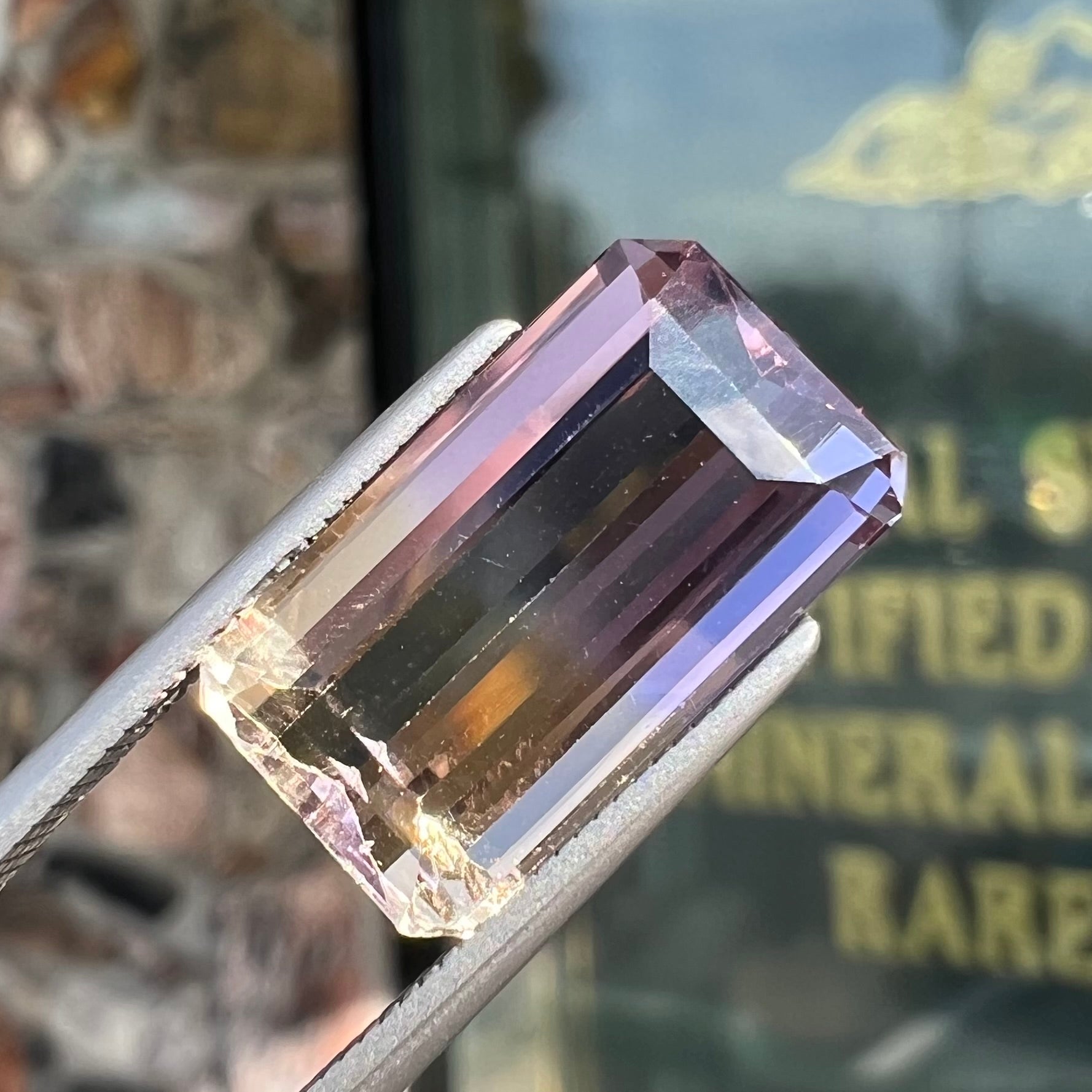 A loose, emerald cut ametrine stone.  The color fades from light purple to light yellow.