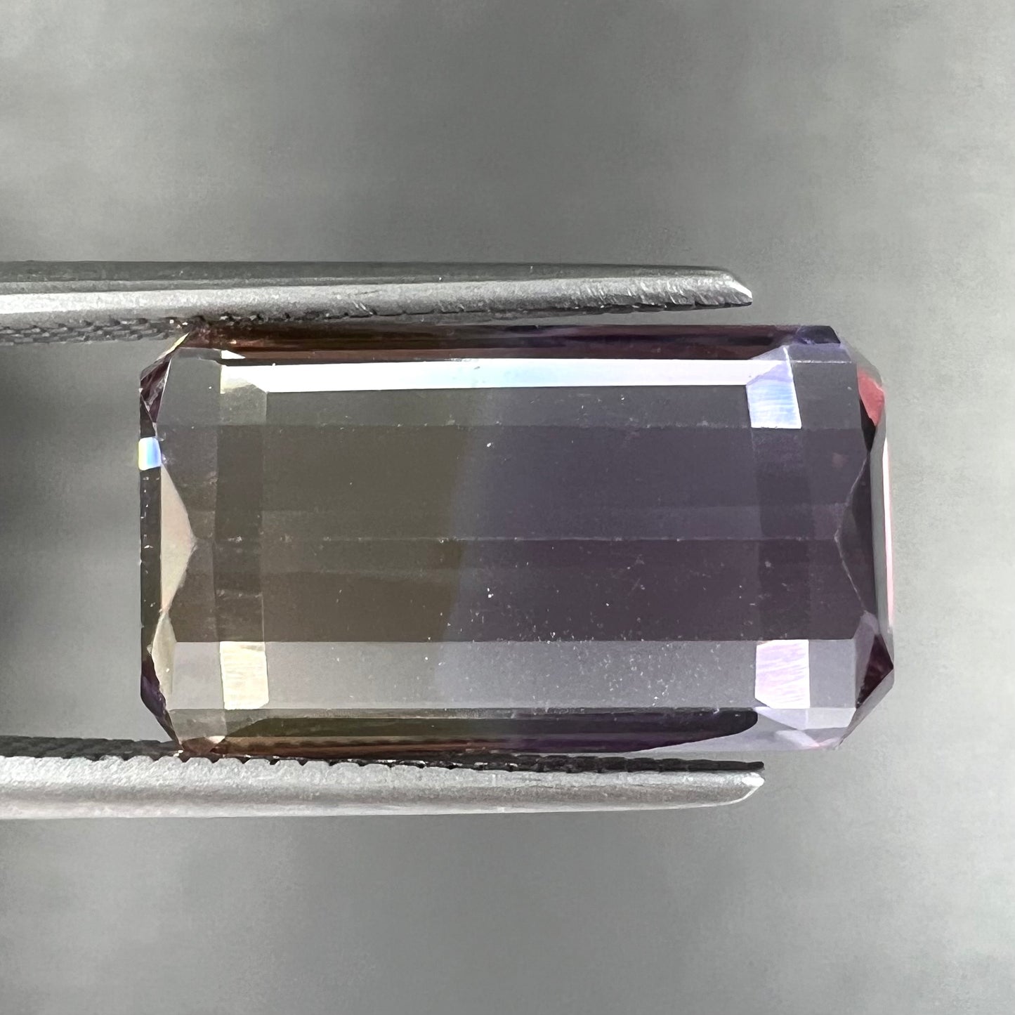 A loose, emerald cut ametrine stone.  The color fades from light purple to light yellow.