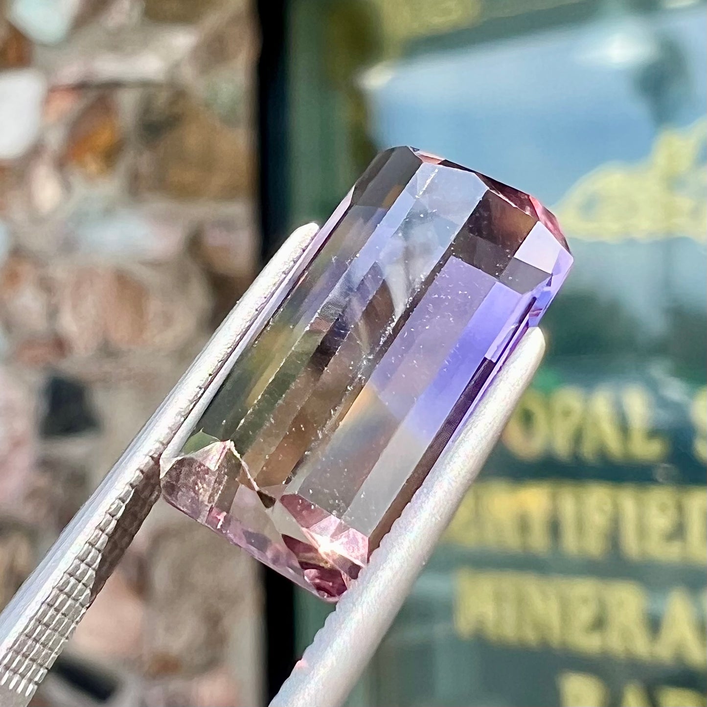 A loose, emerald cut ametrine stone.  The color fades from light purple to light yellow.