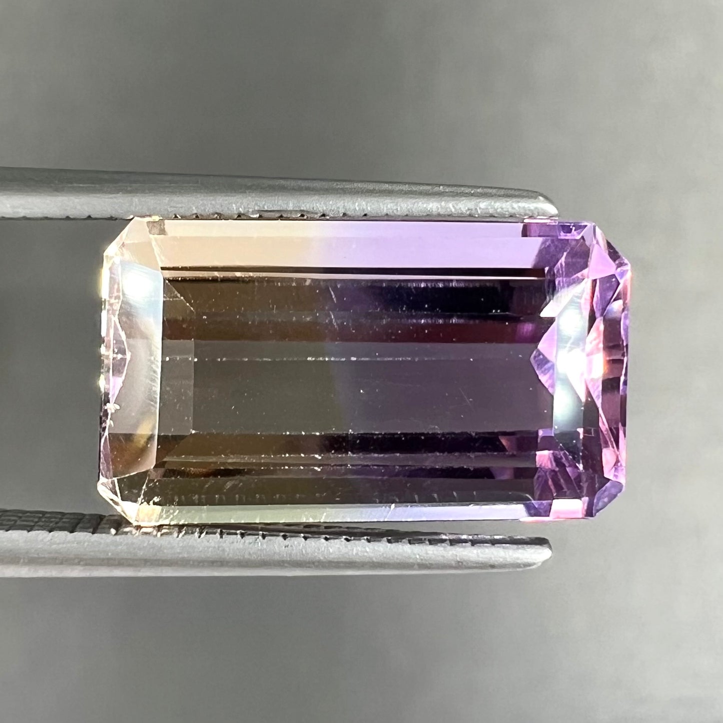 A loose, emerald cut ametrine stone.  The color fades from light purple to light yellow.