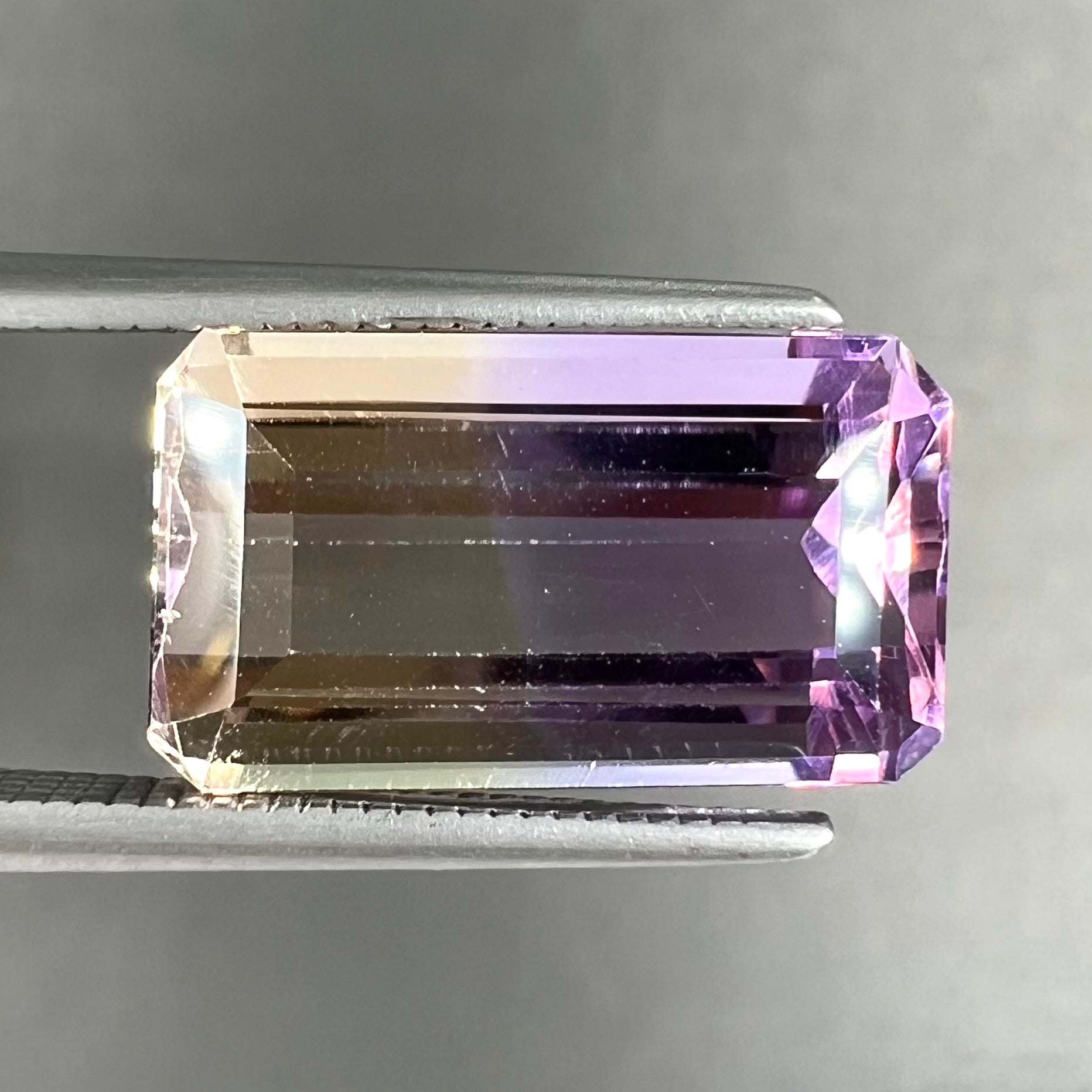 A loose, emerald cut ametrine stone.  The color fades from light purple to light yellow.