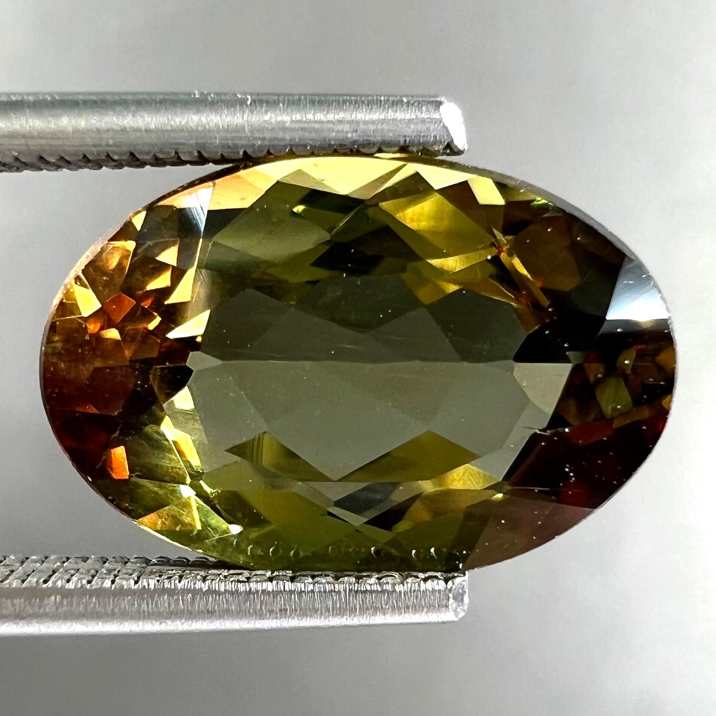A loose, faceted oval cut andalusite gemstone.  The stone shows brown and green colors.