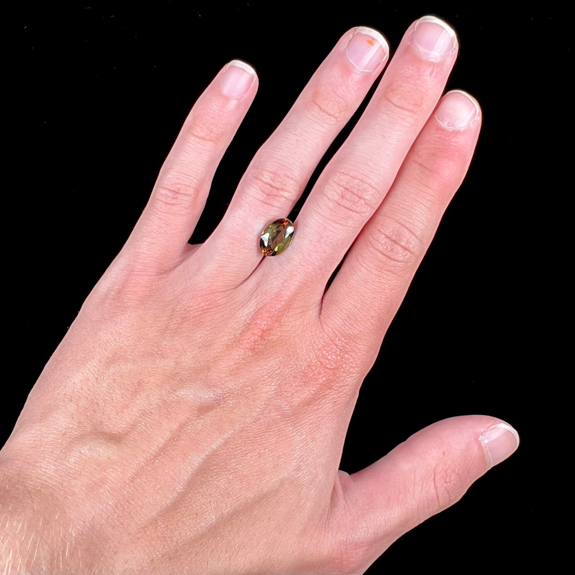 A loose, faceted oval cut andalusite gemstone.  The stone shows brown and green colors.