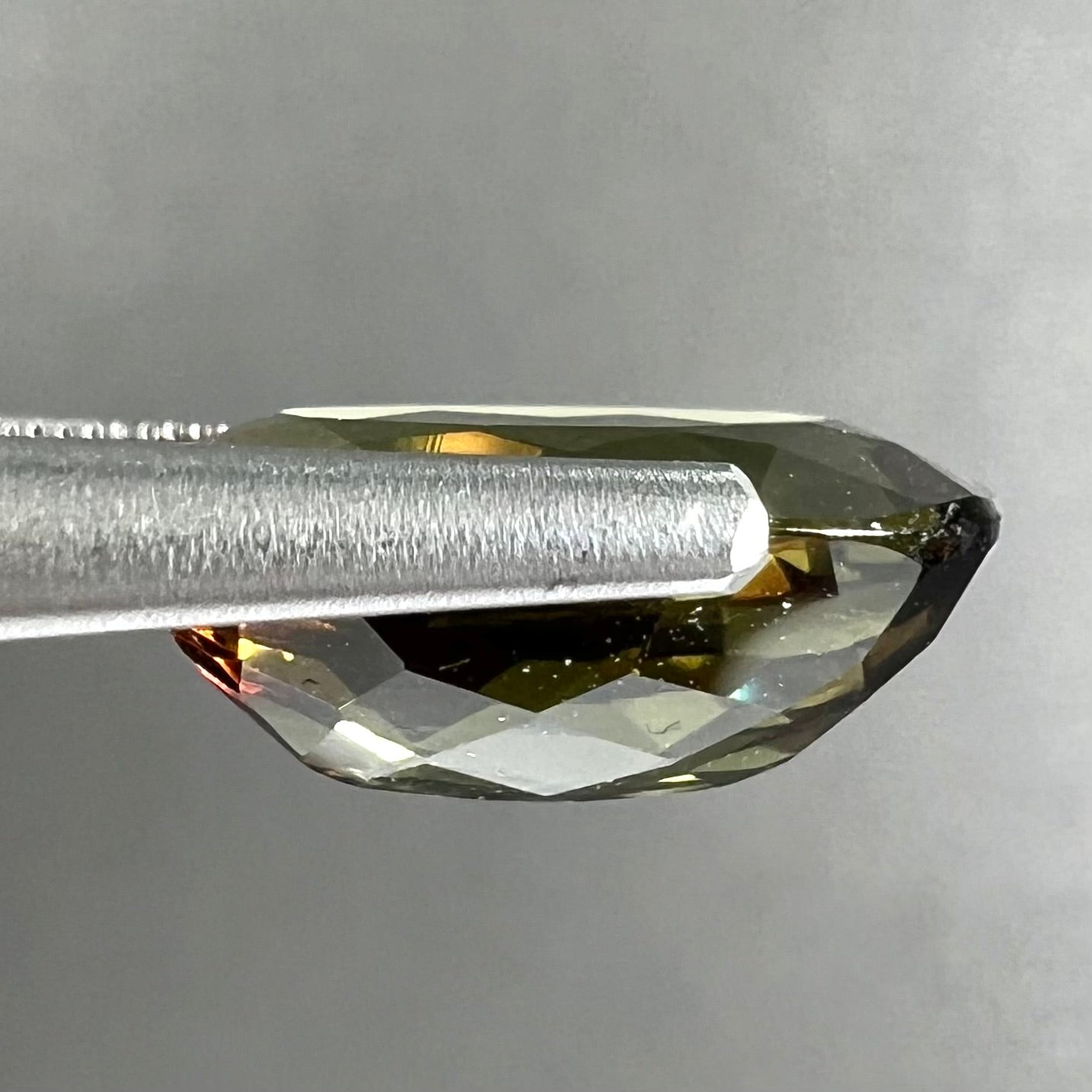A loose, faceted oval cut andalusite gemstone.  The stone shows brown and green colors.