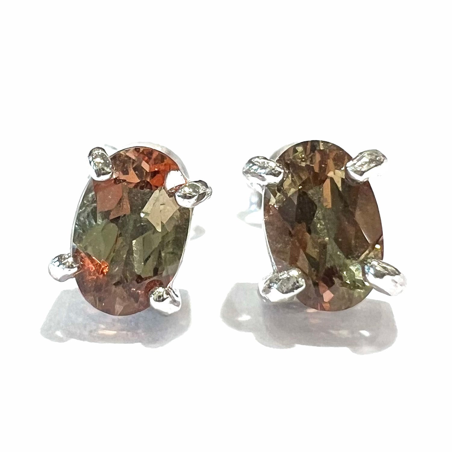 A pair of sterling silver stud earrings prong set with oval cut andalusite stones.