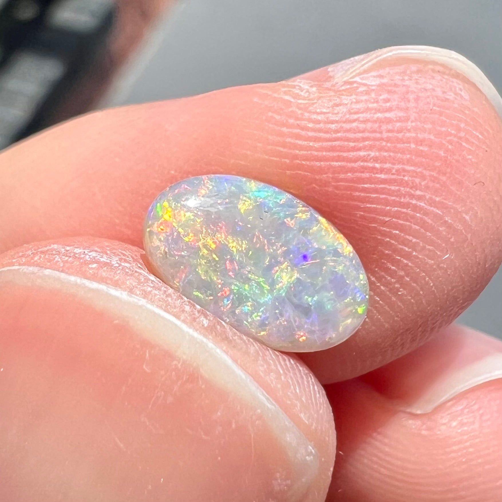 A loose, oval cabochon cut semi-black opal stone from Lightning Ridge, Australia.