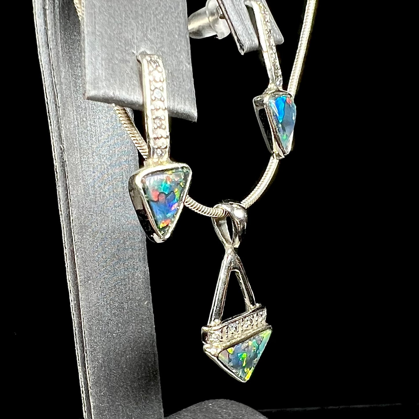 A white gold pendant and earrings set mounted with triangle cut natural black opals and diamonds.