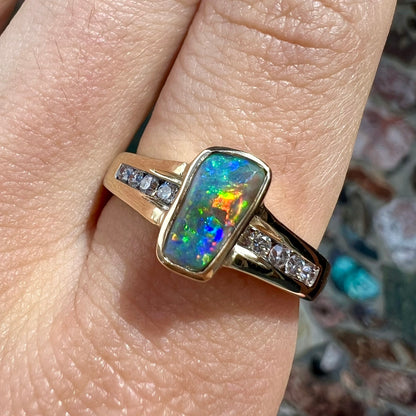 A ladies' yellow gold Australian black crystal opal ring channel set with diamond accent stones.