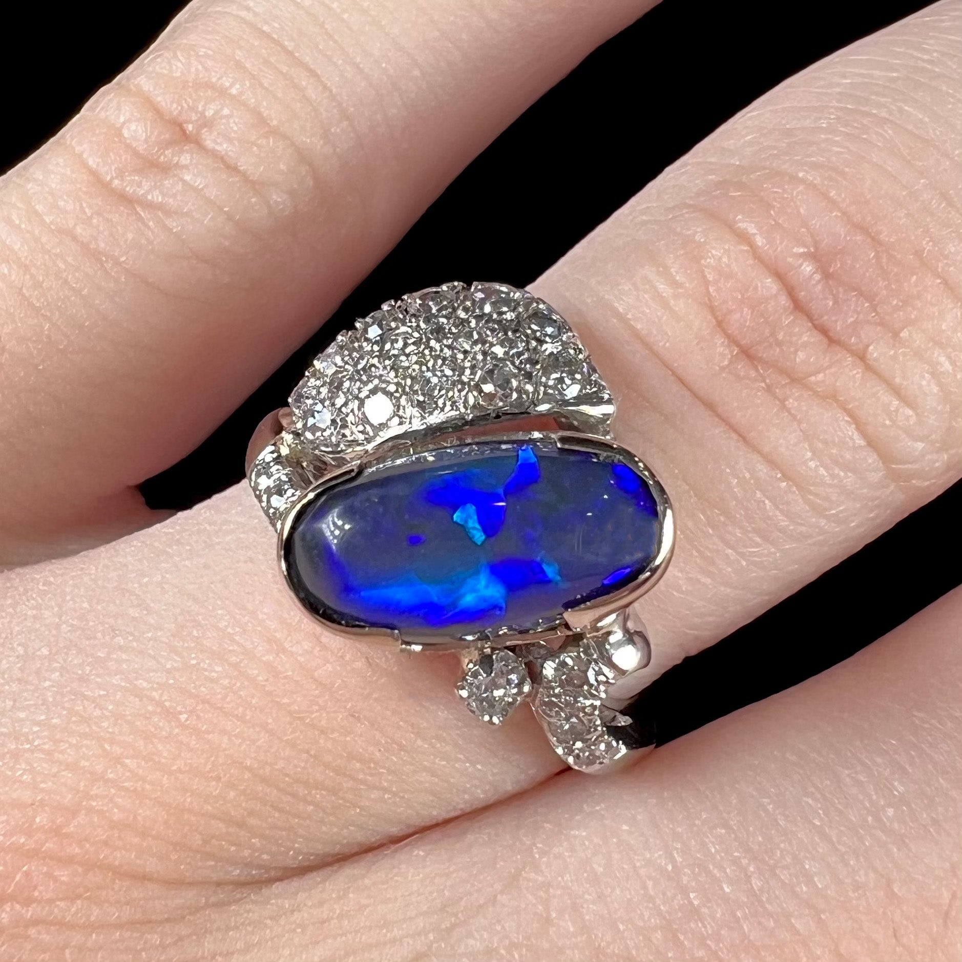 A platinum ring set with an oval cut black opal and round cut diamonds in a leaf design.