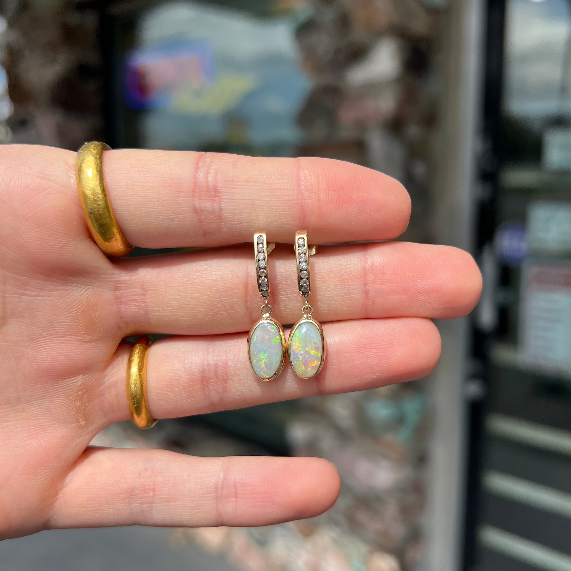 A pari of yellow gold dangle earrings set with natural white crystal opals and diamond accents.