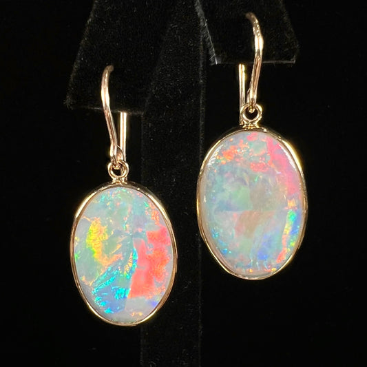 A pair of yellow gold earrings bezel set with oval cabochon cut natural opal stones.