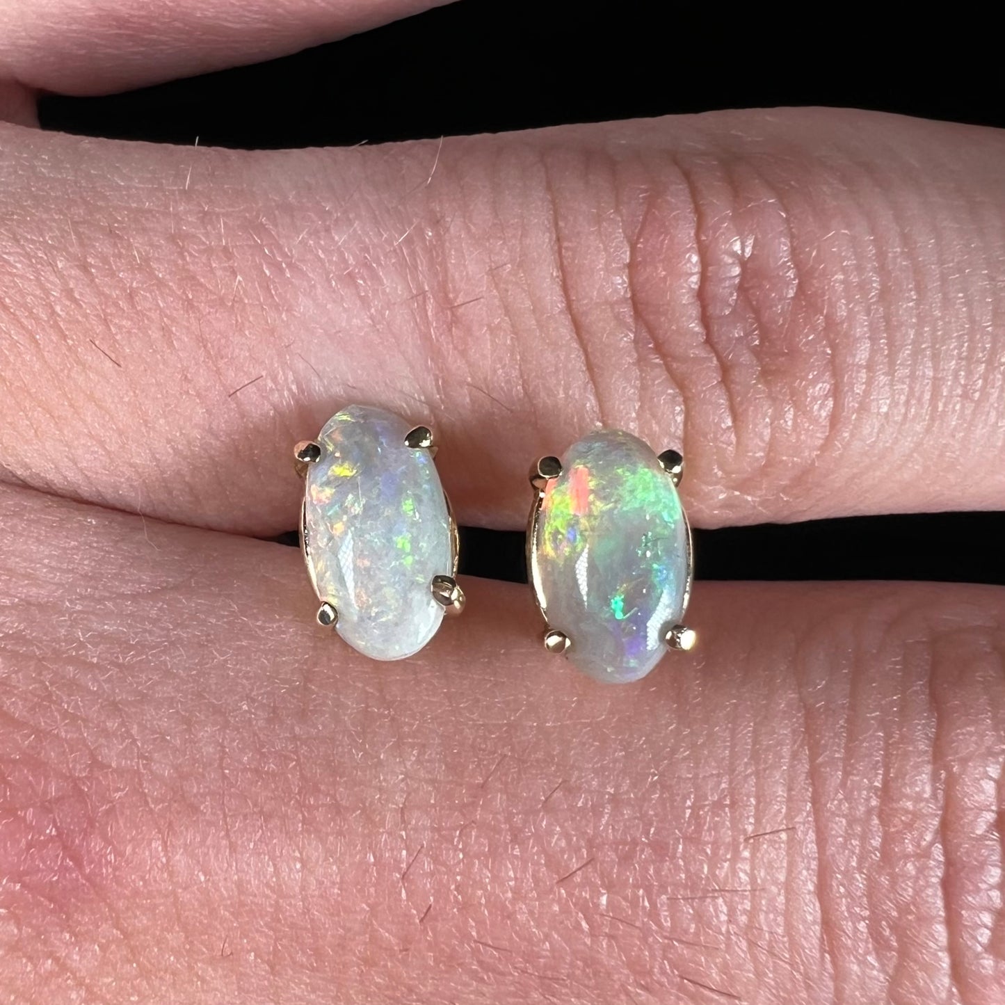 A pair of natural, semi-black crystal opal stud earrings in yellow gold.  The opals are oval cabochon cut.
