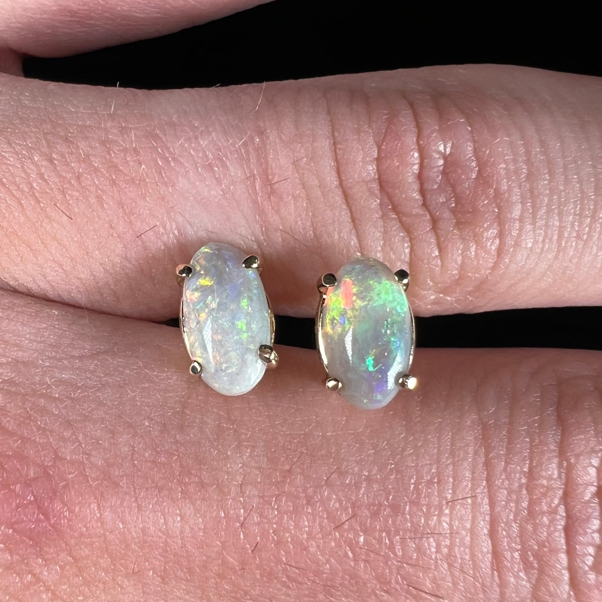 A pair of natural, semi-black crystal opal stud earrings in yellow gold.  The opals are oval cabochon cut.