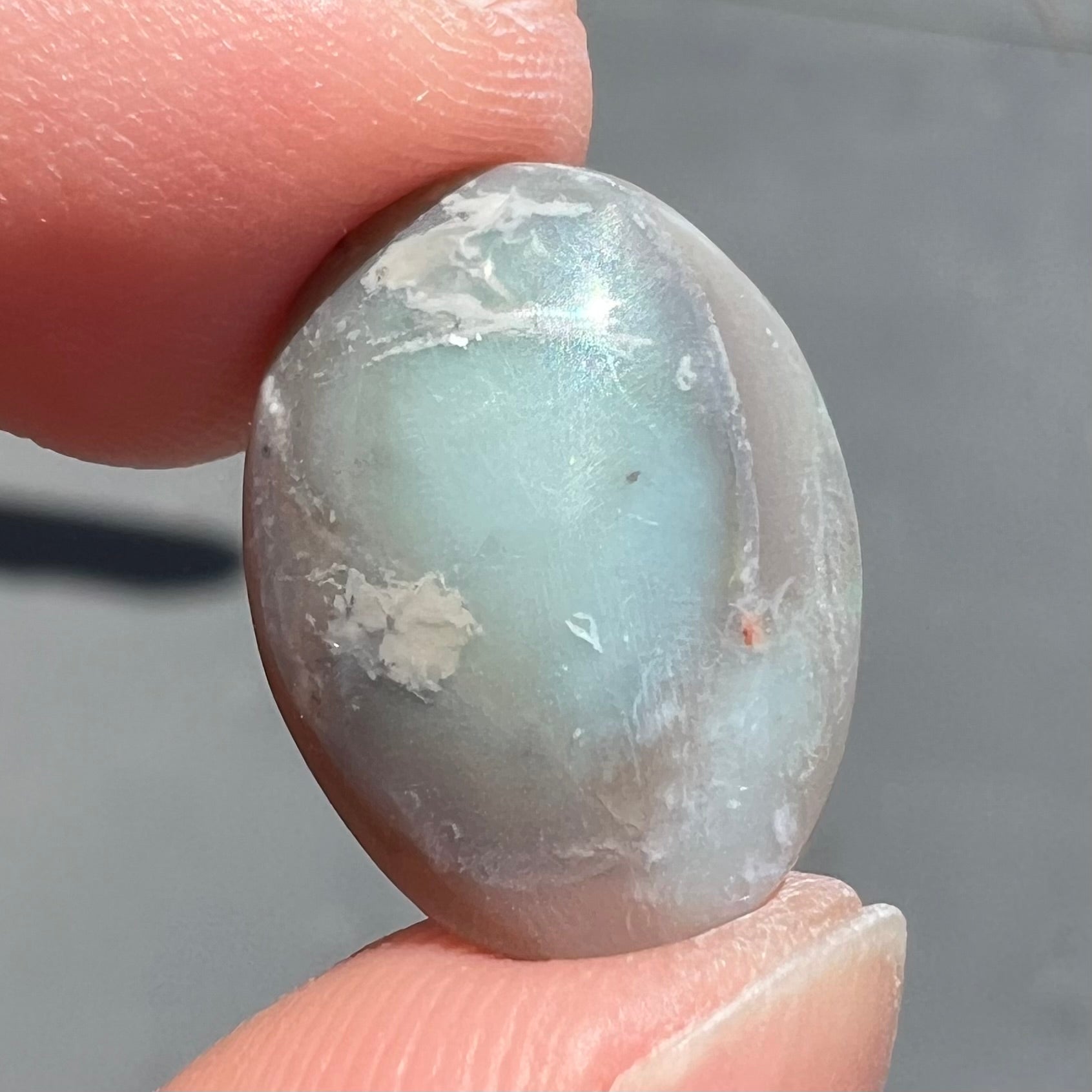 A loose, oval cut light opal stone from Mintabie, Australia.  The stone shows dull orange and green colors.