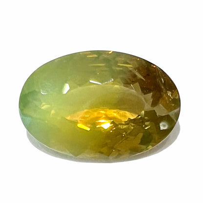 A loose, faceted oval cut bicolor chrysoberyl stone.  The stone goes from neon green to dark green with orangey red flashes.