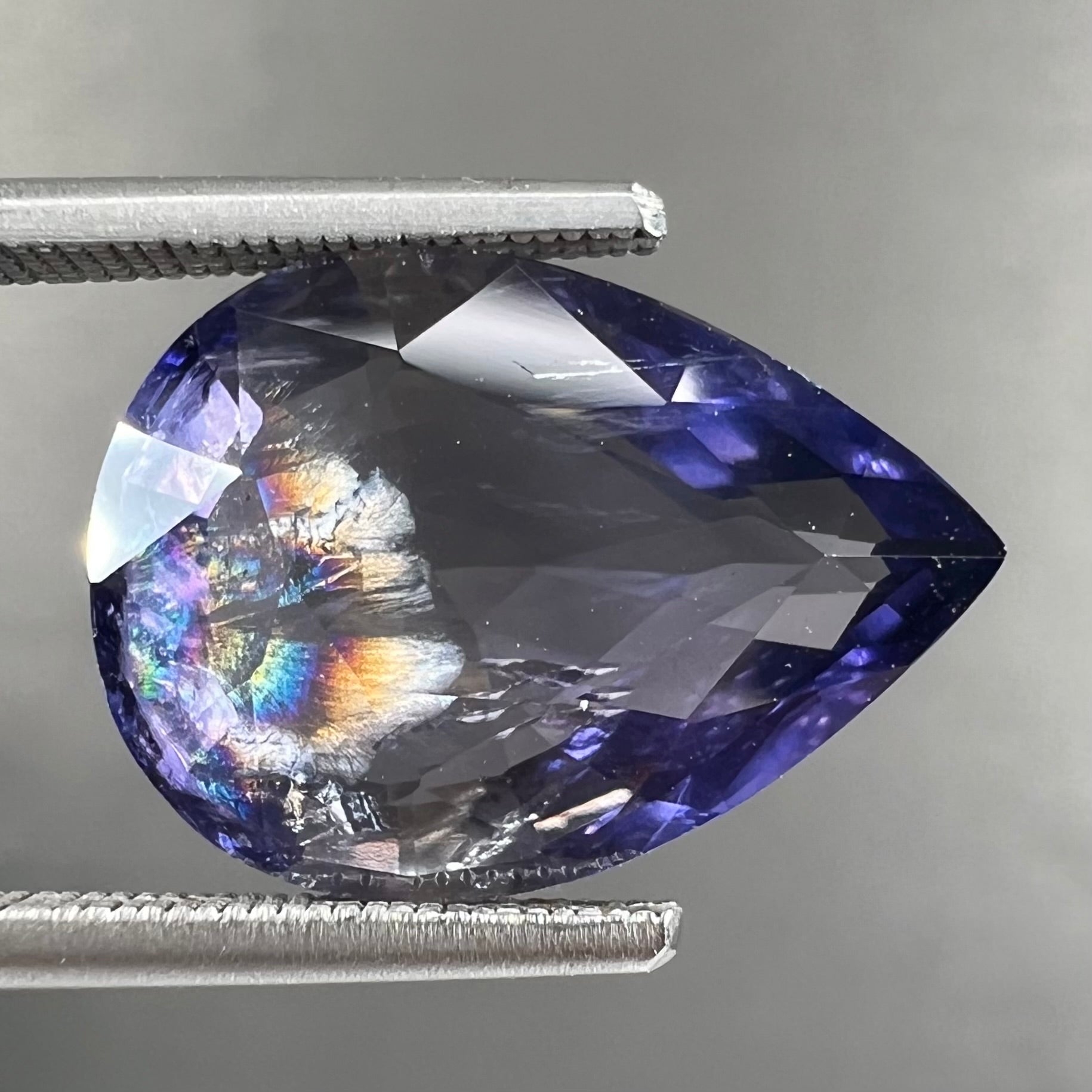 A loose, pear shaped bicolor iolite gemstone.  The stone shows violite purple and silver colors.