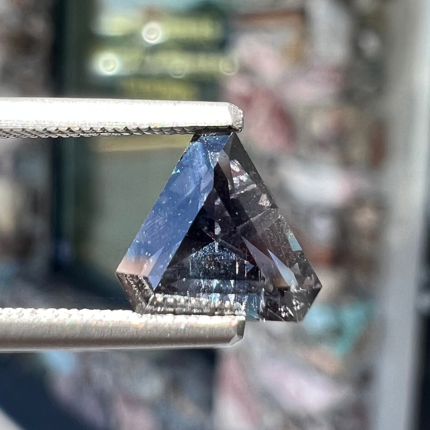 A loose, modified triangle cut parti sapphire gemstone.  The sapphire shows colors of blue, violet, purple, and gray.