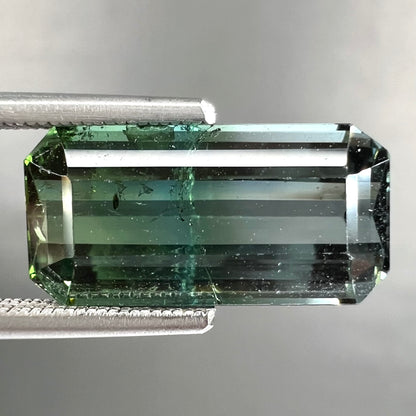 A loose, emerald cut bicolor tourmaline stone.  The colors blend from green to blue-green to sttel blue.