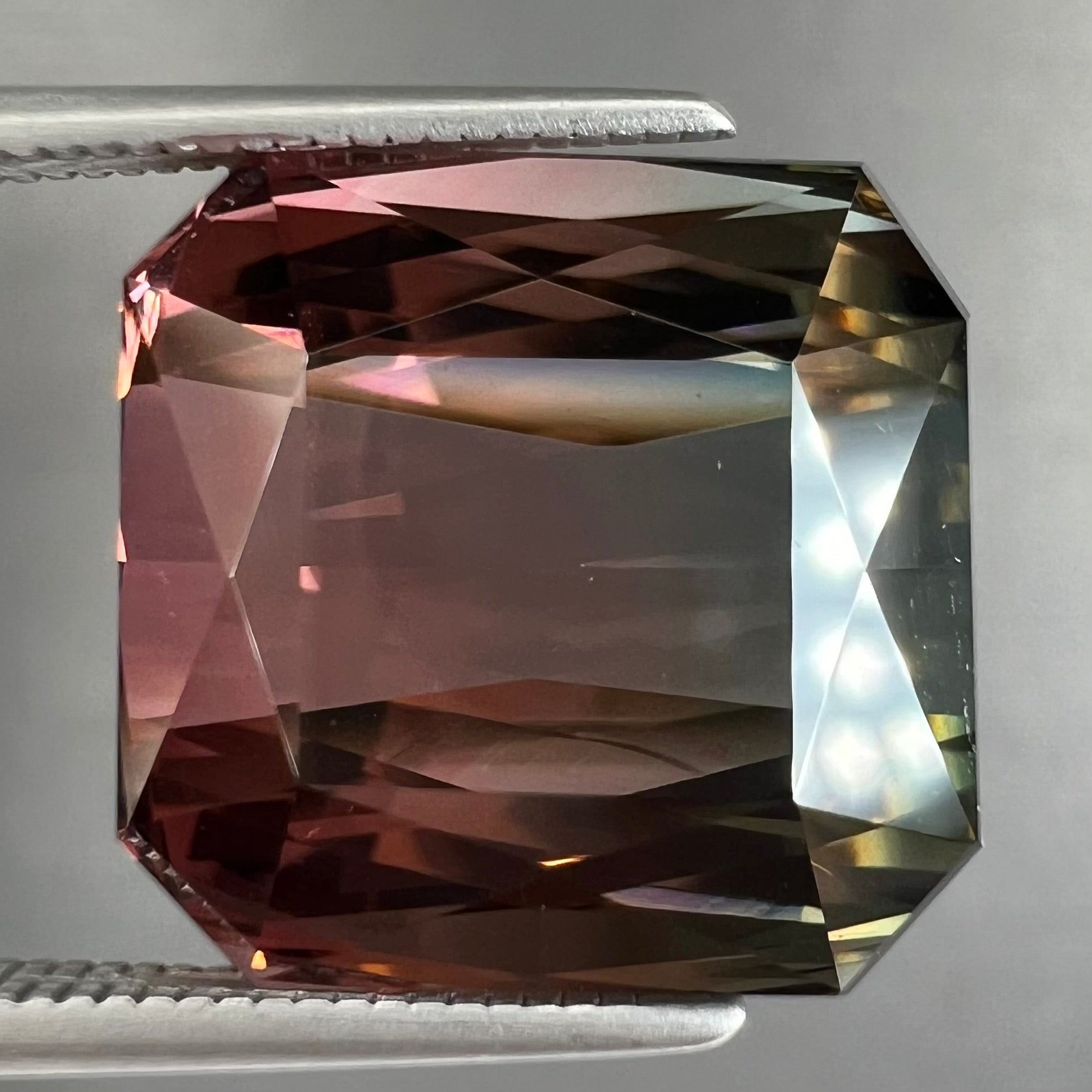 A loose, faceted modified emerald cut bicolor tourmaline gemstone.  The stone transitions from dark pink to dark green colors.