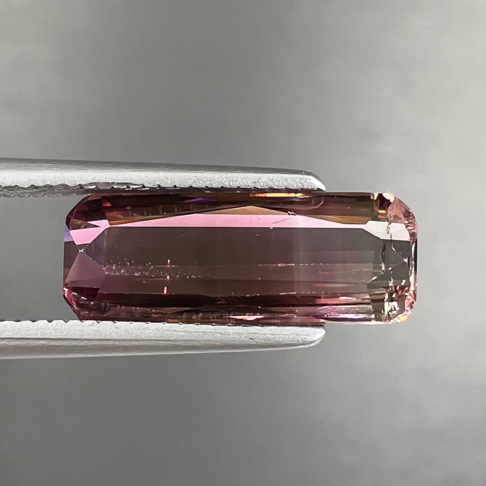 A loose, modified emerald cut tricolor tourmaline.  The stone transitions from pink to light pink to white colors.