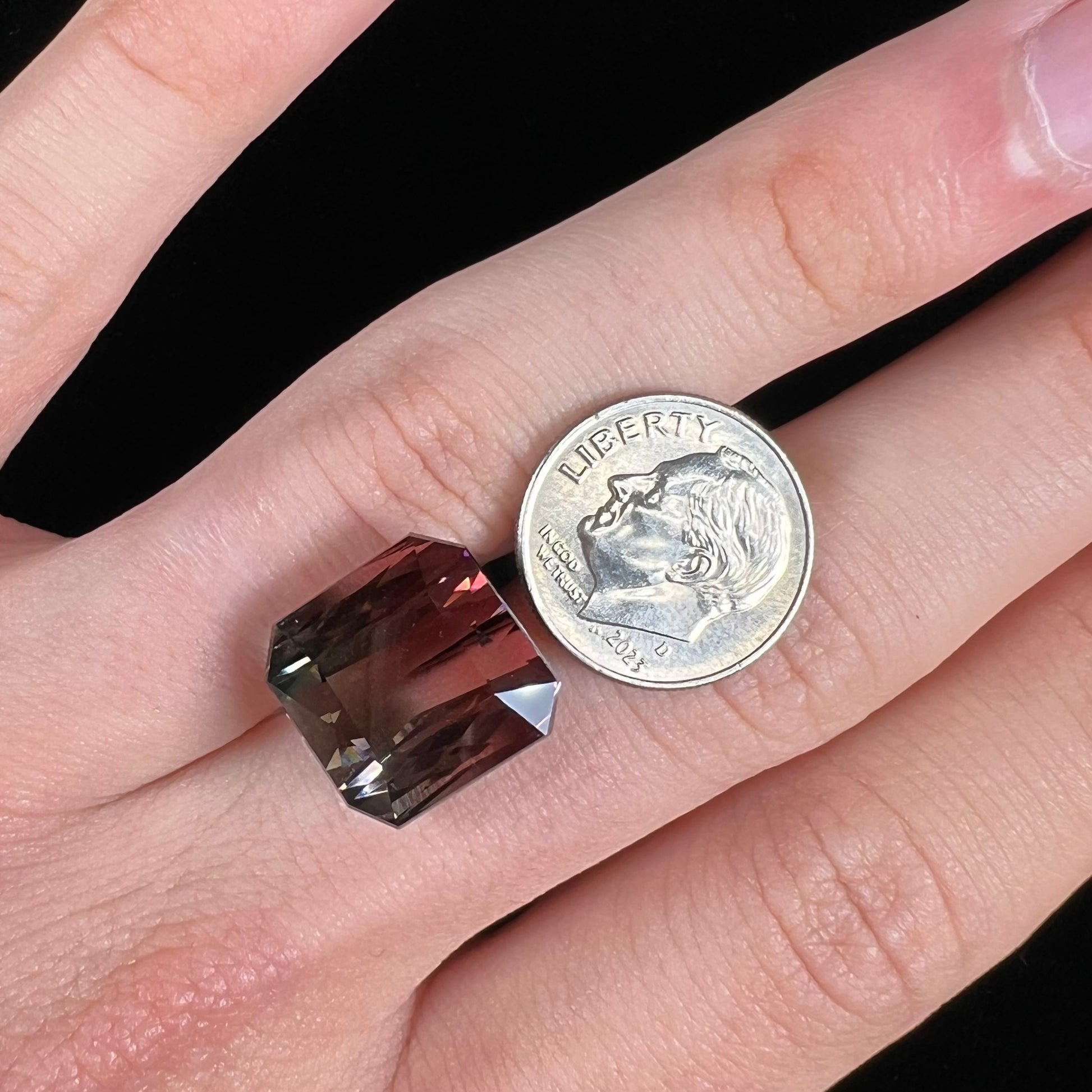A loose, faceted modified emerald cut bicolor tourmaline gemstone.  The stone transitions from dark pink to dark green colors.