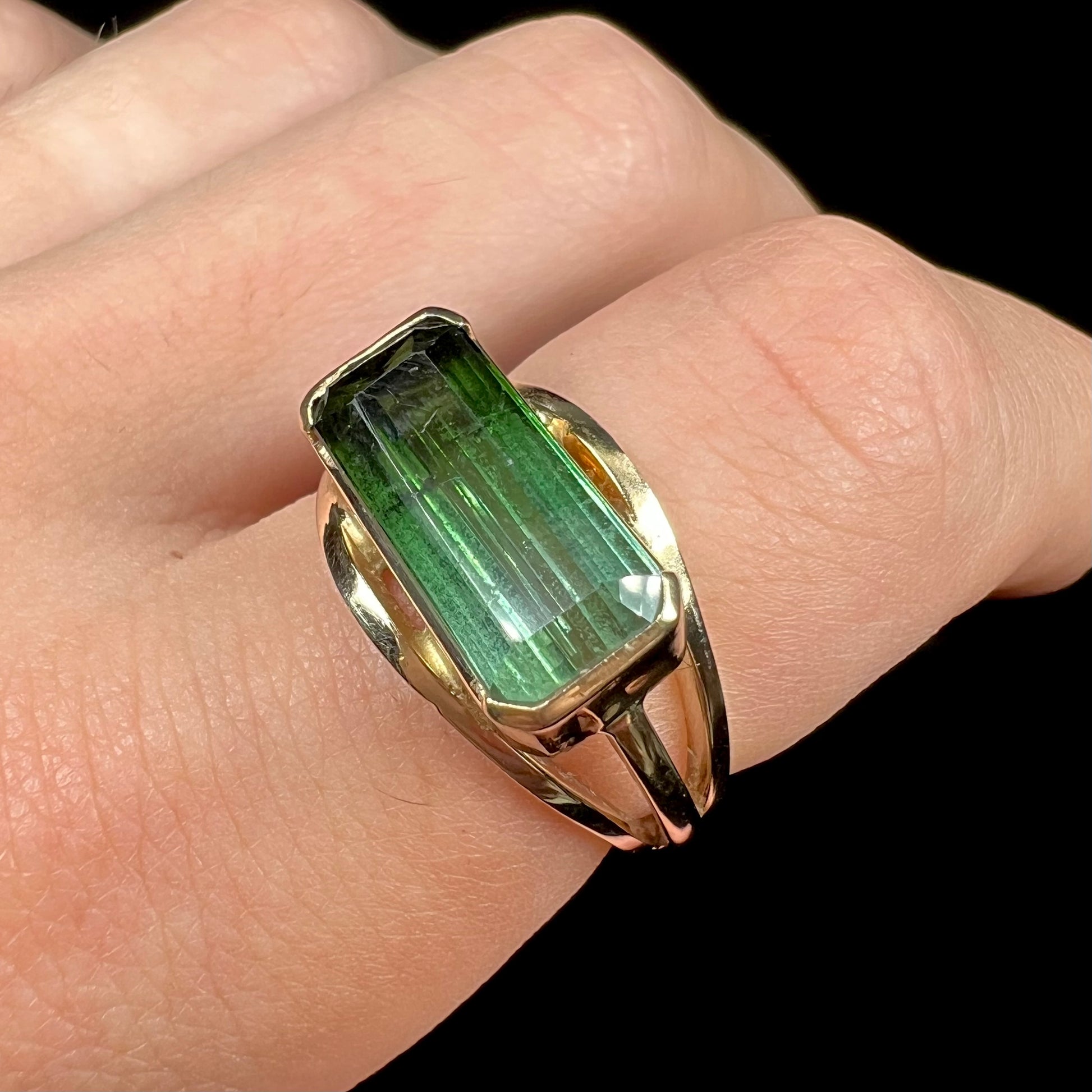 A men's emerald cut tricolor tourmaline solitaire ring in yellow gold.  The tourmaline shifts from green to blue green to blue.