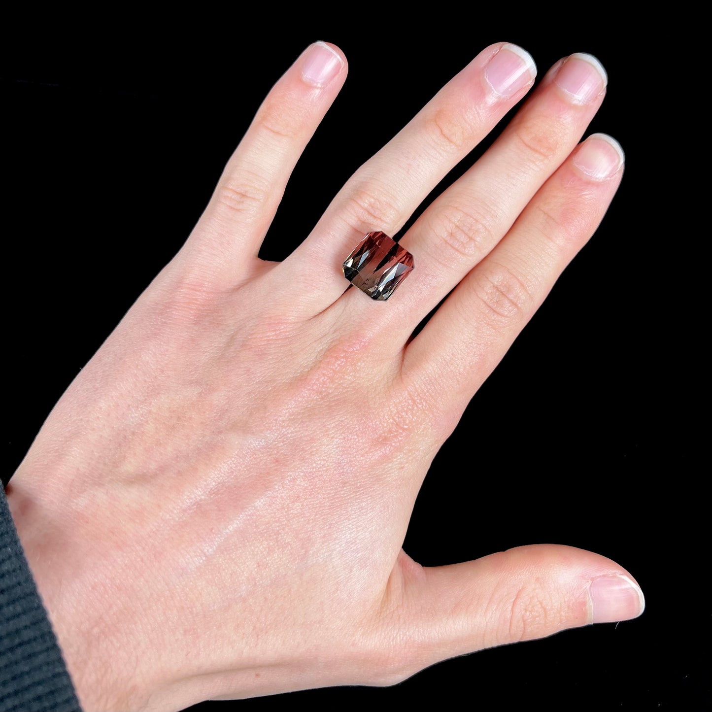 A loose, faceted modified emerald cut bicolor tourmaline gemstone.  The stone transitions from dark pink to dark green colors.