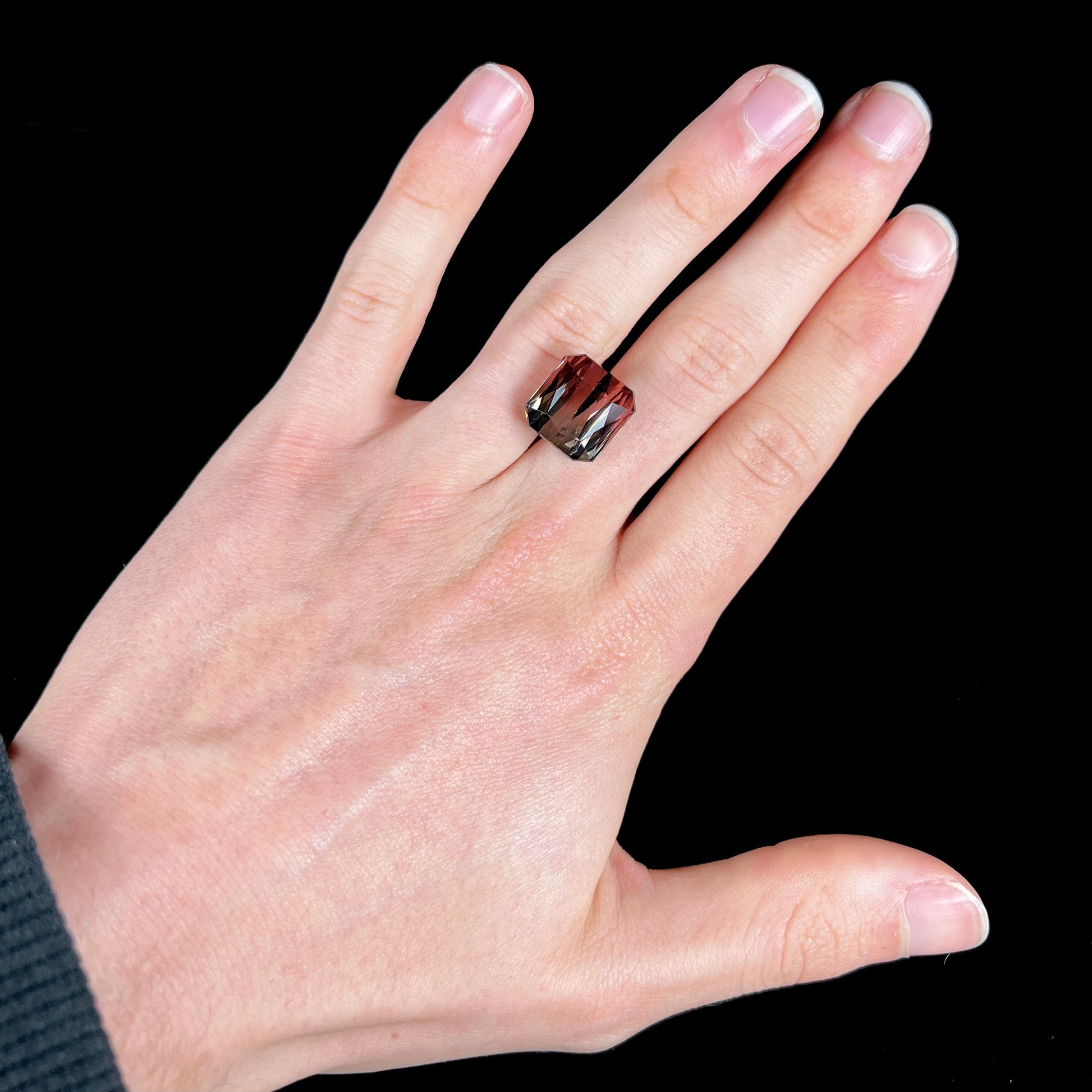 A loose, faceted modified emerald cut bicolor tourmaline gemstone.  The stone transitions from dark pink to dark green colors.
