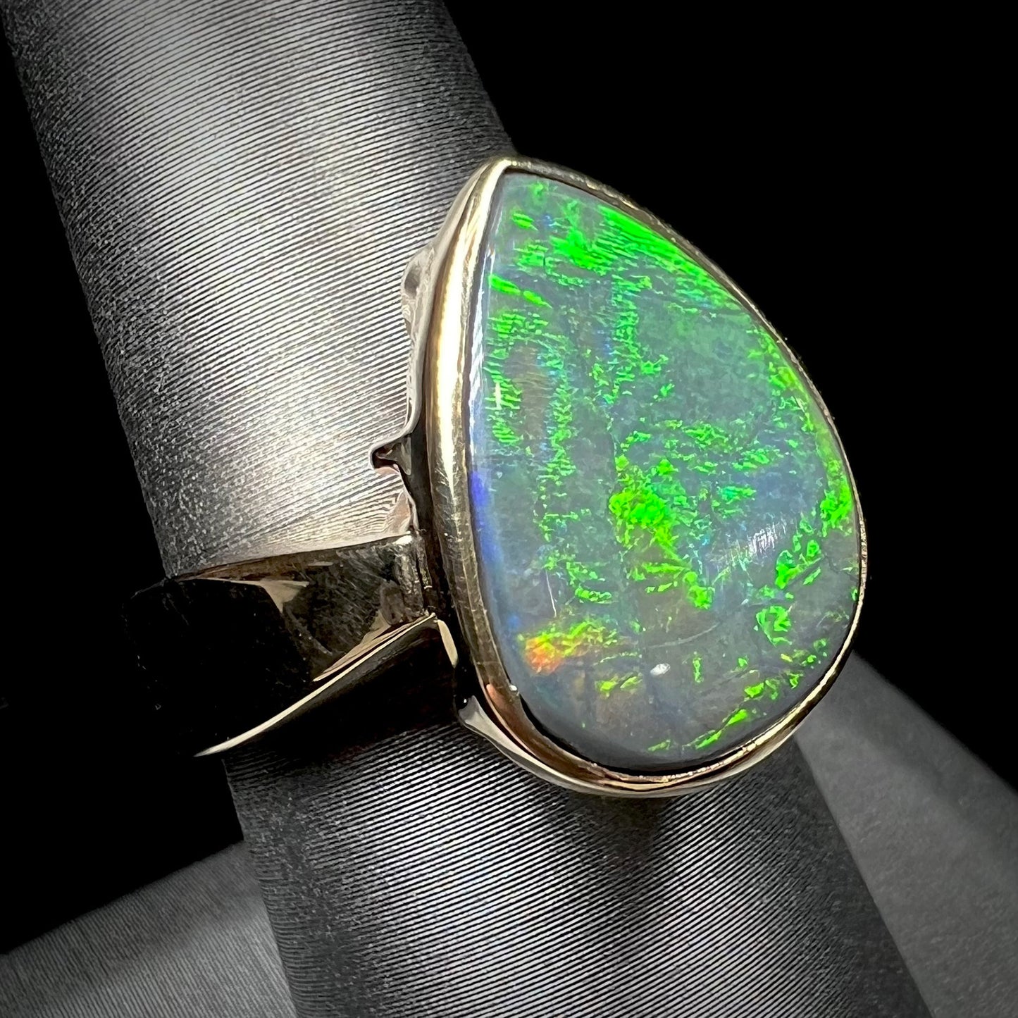 A large ladies' yellow gold solitaire ring set with a natural, pear shaped black crystal opal.  The opal has green and orange fire.