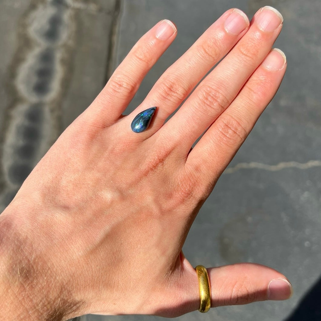 A freeform pear shaped black opal from Lightning Ridge, Australia.