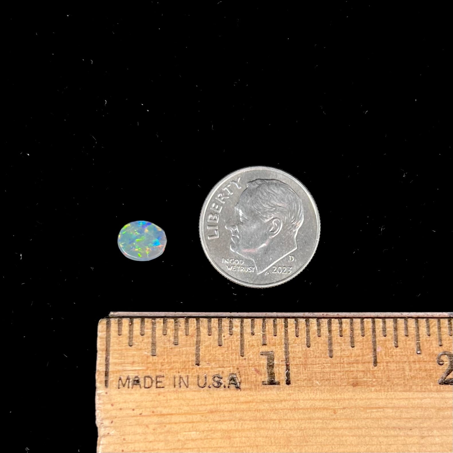 A loose oval cabochon cut black opal from Lightning Ridge, Australia.  The opal shows green and red colors.