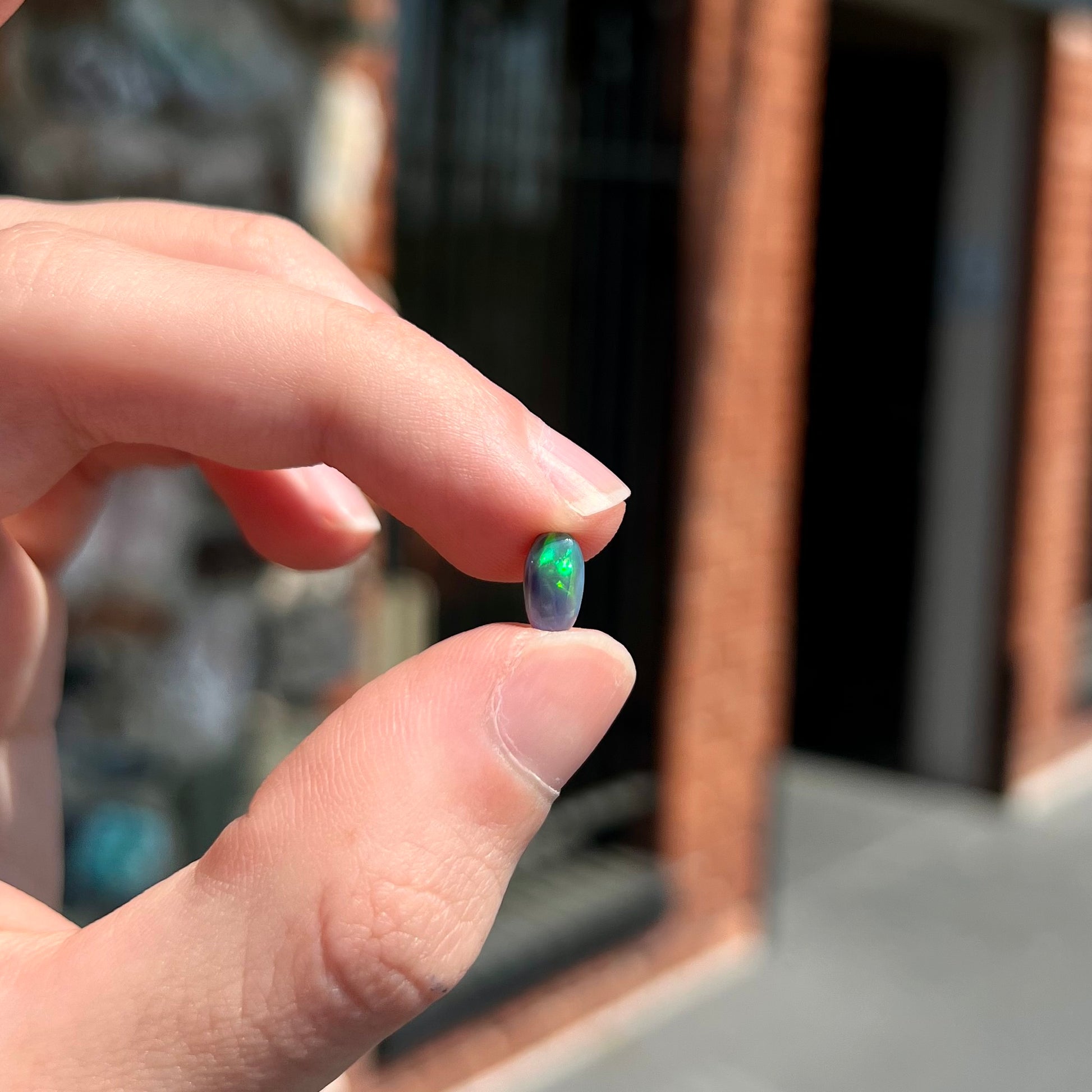 A loose, pill shaped black opal stone from Lightning Ridge, Australia.  The opal is green and blue.