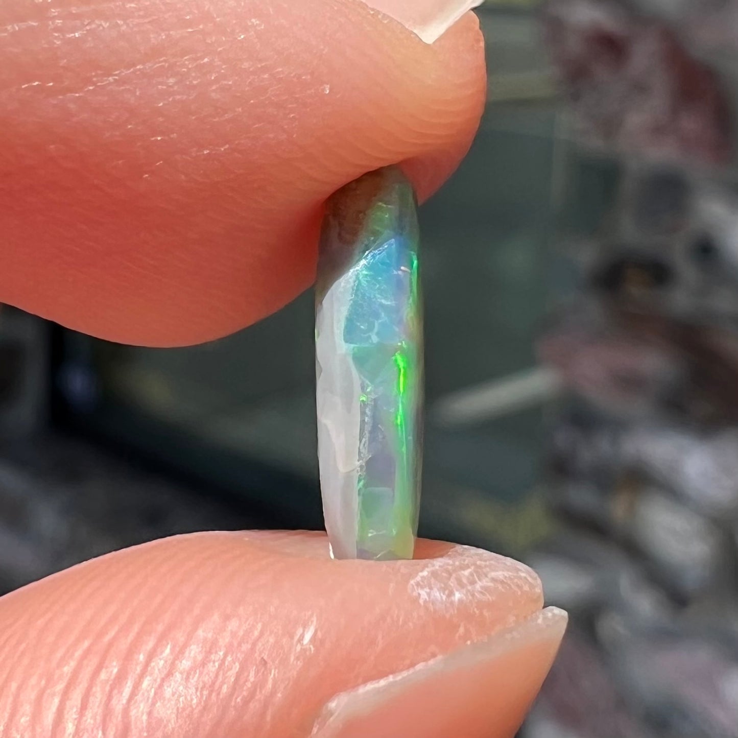 A loose, oval cabochon cut semi-black opal from Lightning Ridge, Australia.  The opal plays green and orange colors.