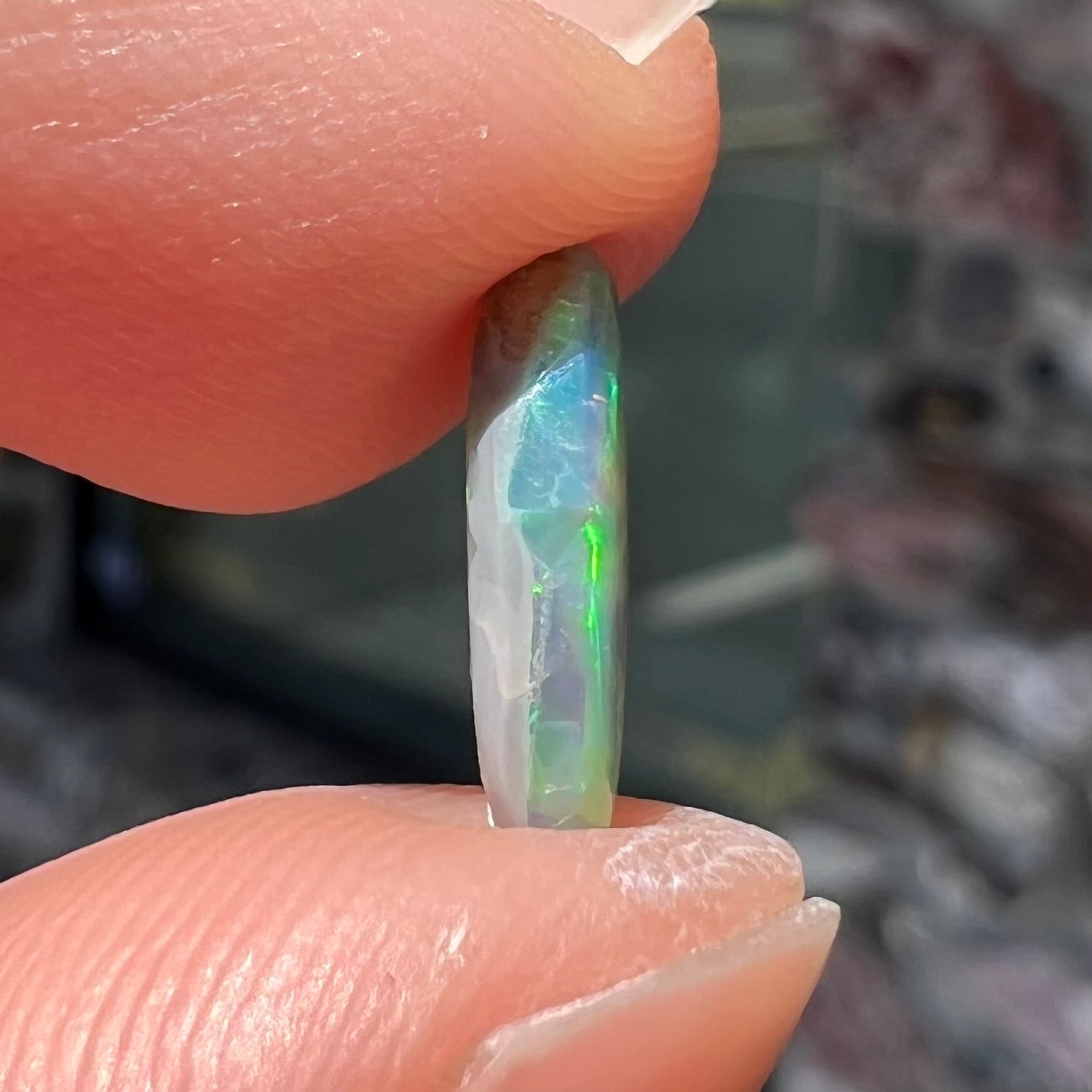 A loose, oval cabochon cut semi-black opal from Lightning Ridge, Australia.  The opal plays green and orange colors.