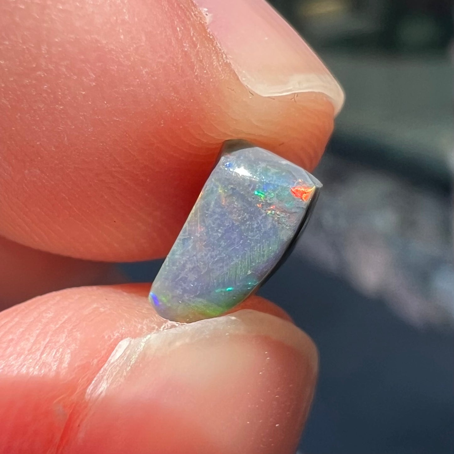 A freeform shaped black opal stone from Lightning Ridge, Australia.