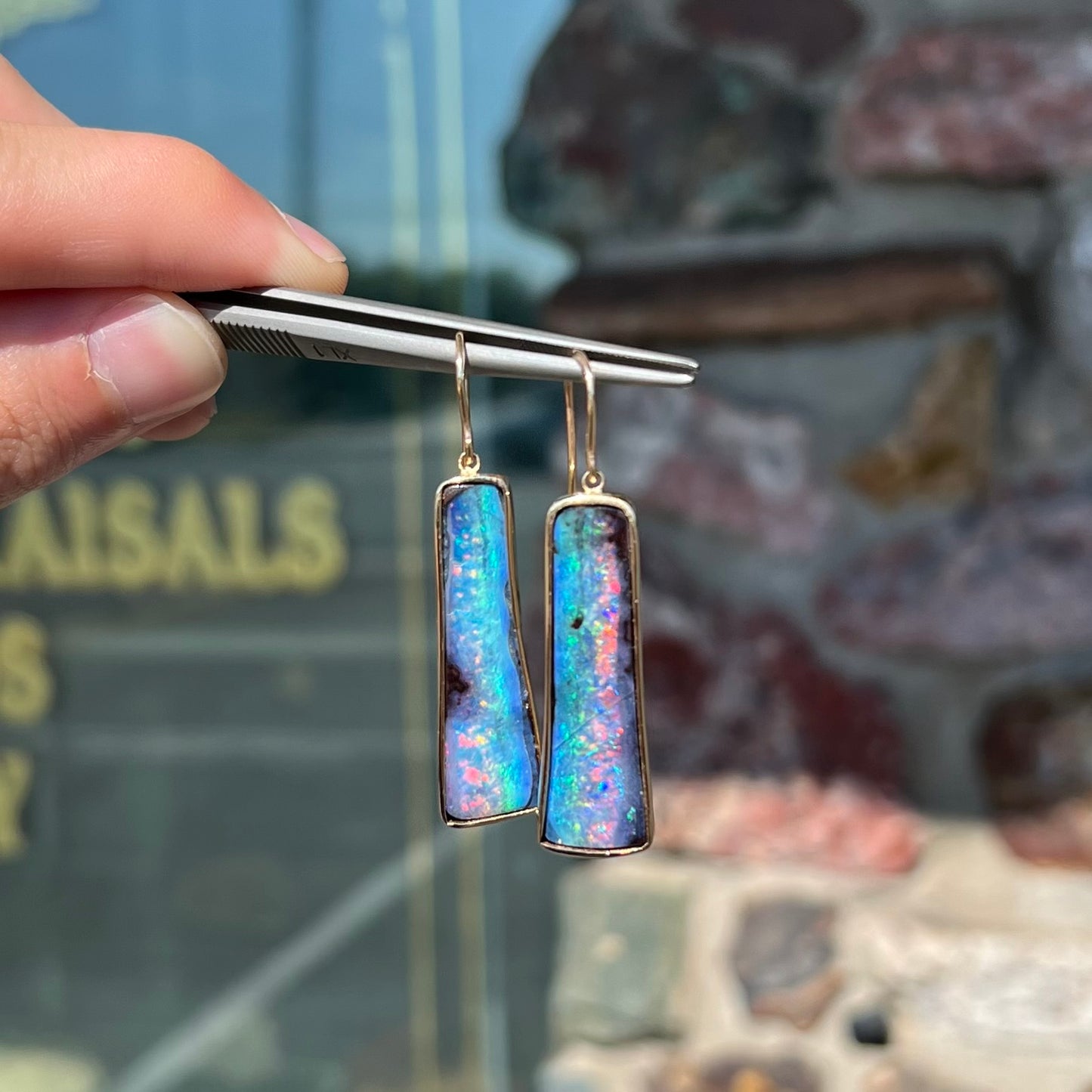 A pair of natural boulder opal dangle earrings set in yellow gold.  The opal displays a rainbow of colors and is from Bull Creek, Australia.