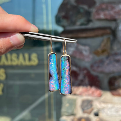 A pair of natural boulder opal dangle earrings set in yellow gold.  The opal displays a rainbow of colors and is from Bull Creek, Australia.