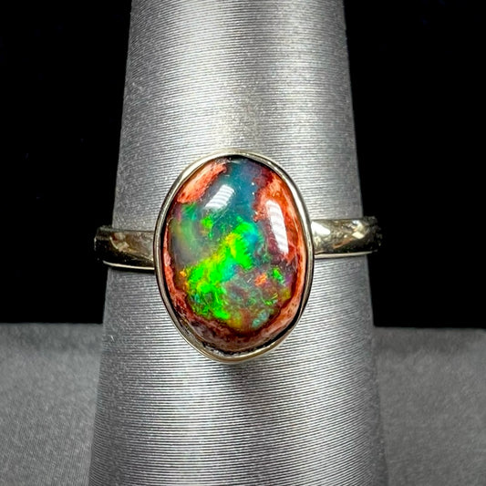 A ladies' yellow gold solitaire ring bezel set with an oval cabochon cut natural black Mexican cantera fire opal stone.