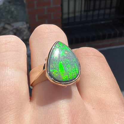 A large ladies' yellow gold solitaire ring set with a natural, pear shaped black crystal opal.  The opal has green and orange fire.