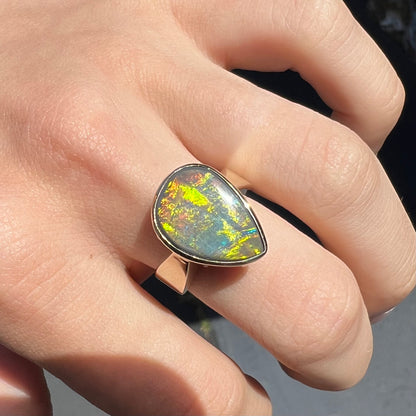 A large ladies' yellow gold solitaire ring set with a natural, pear shaped black crystal opal.  The opal has green and orange fire.