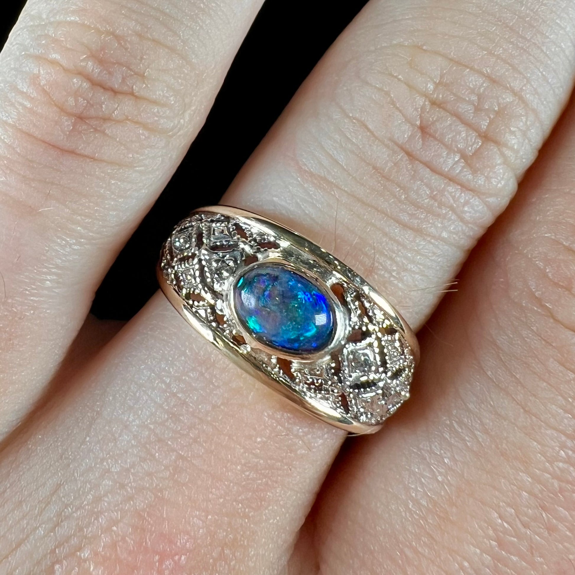 A ladies' yellow gold filigree style ring set with a natural black opal and diamond accents.